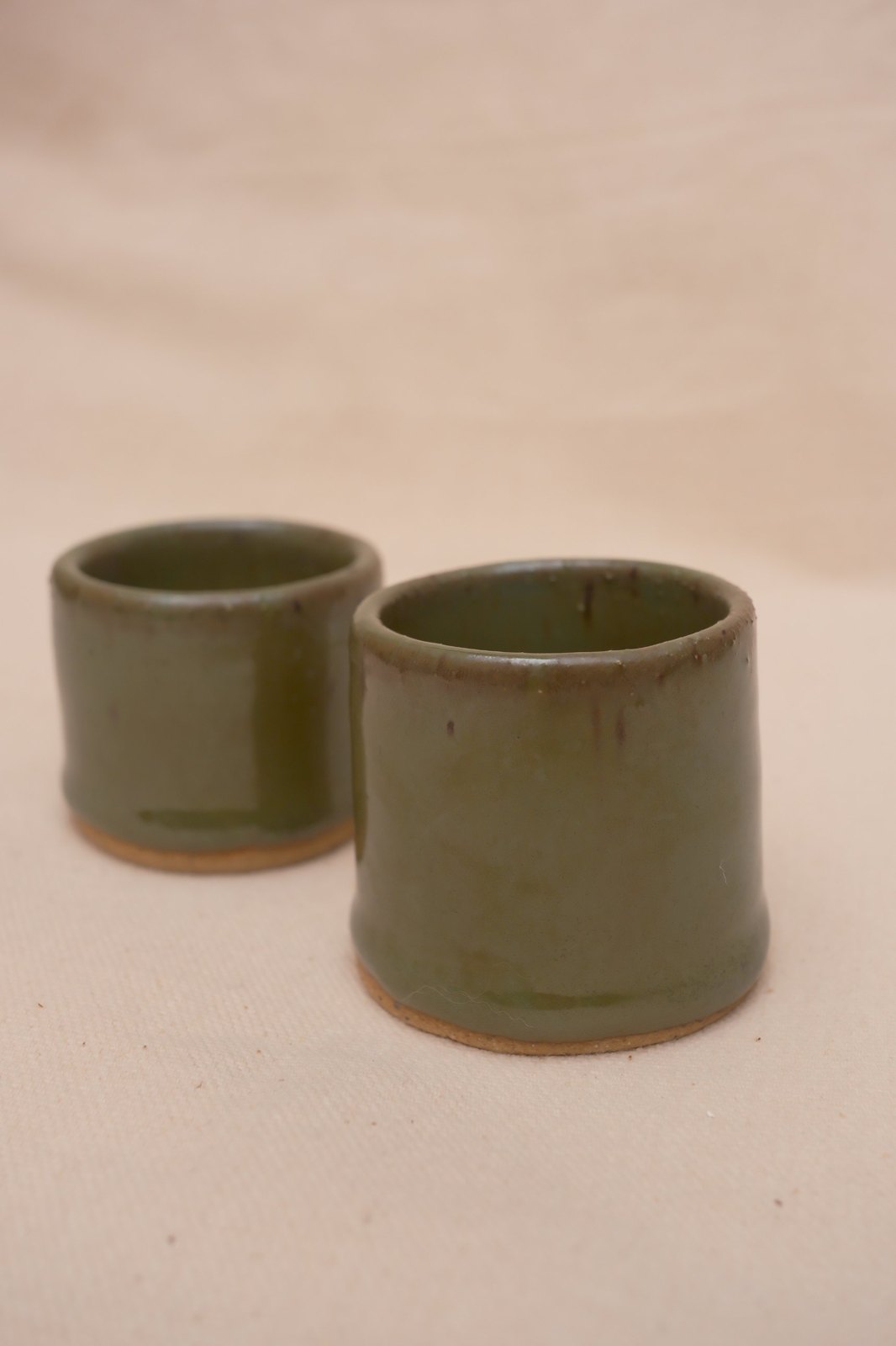 Two olive green shot glasses in Kelp Forest glaze on linen