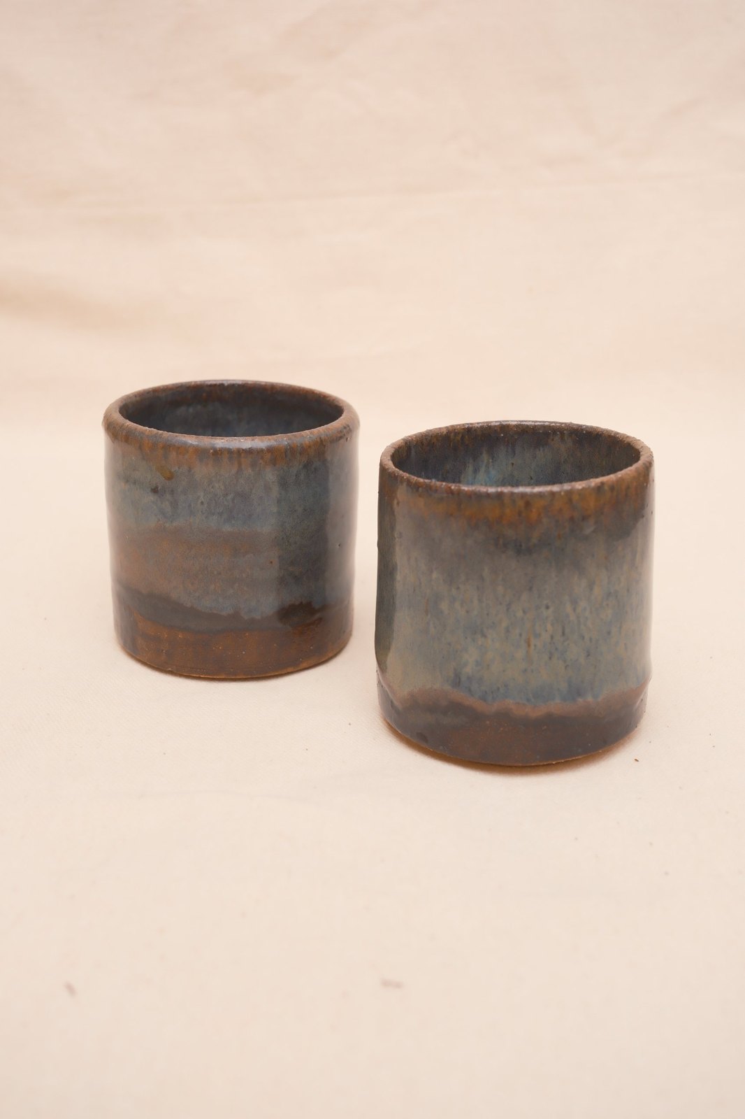 Two espresso cups in a blue-grey glaze over rust-brown, on linen