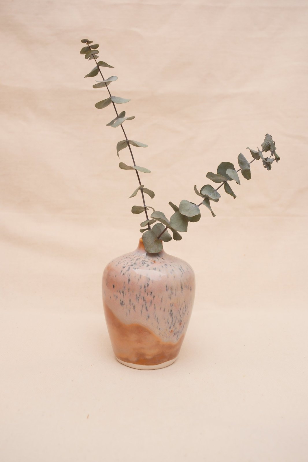 Bud vase, No. 17: pinkish orange with speckled white glaze, holding eucalyptus