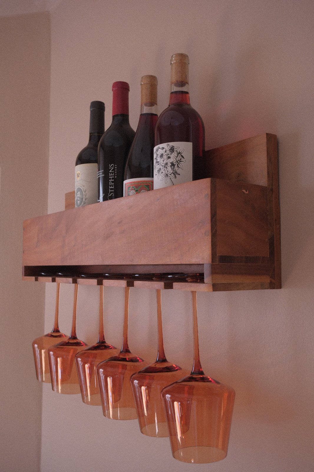 Wooden wine rack with four bottles and six amber stemmed glasses hanging below
