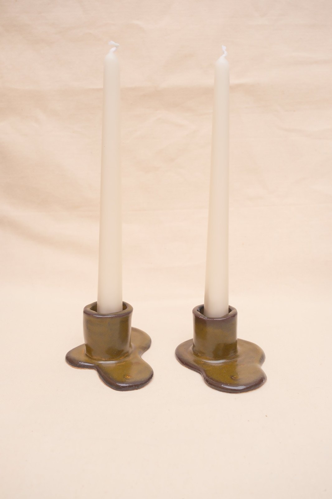 Two Tenmoku candlestick holders with ivory taper candles, on linen