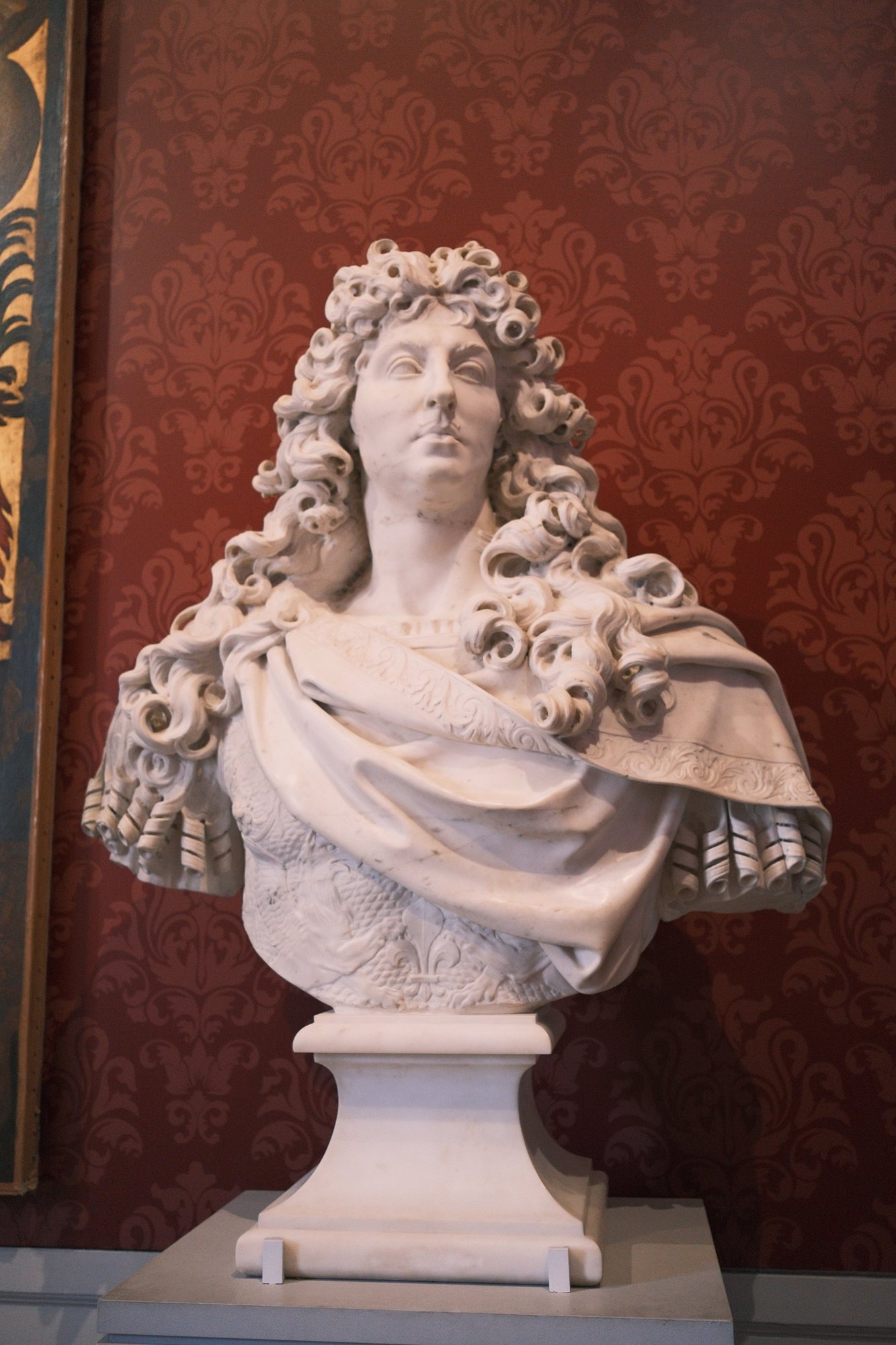 Marble bust with cascading carved curls against red damask wallpaper