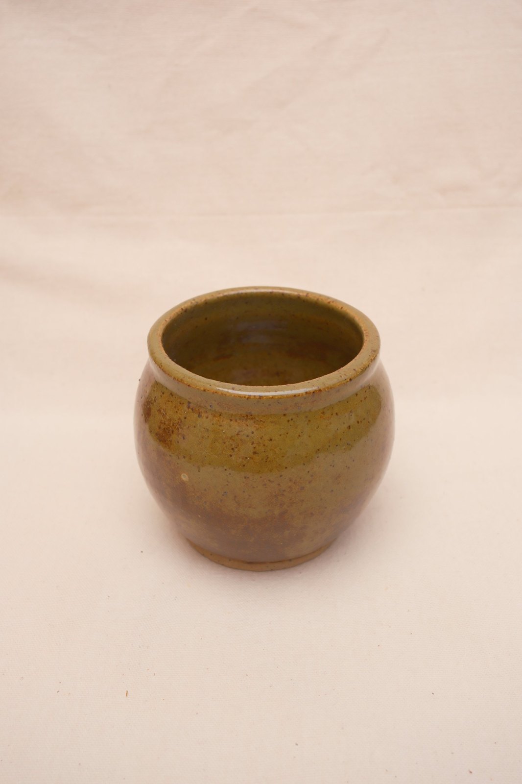 Round-bellied bowl in deep olive speckle glaze, on linen