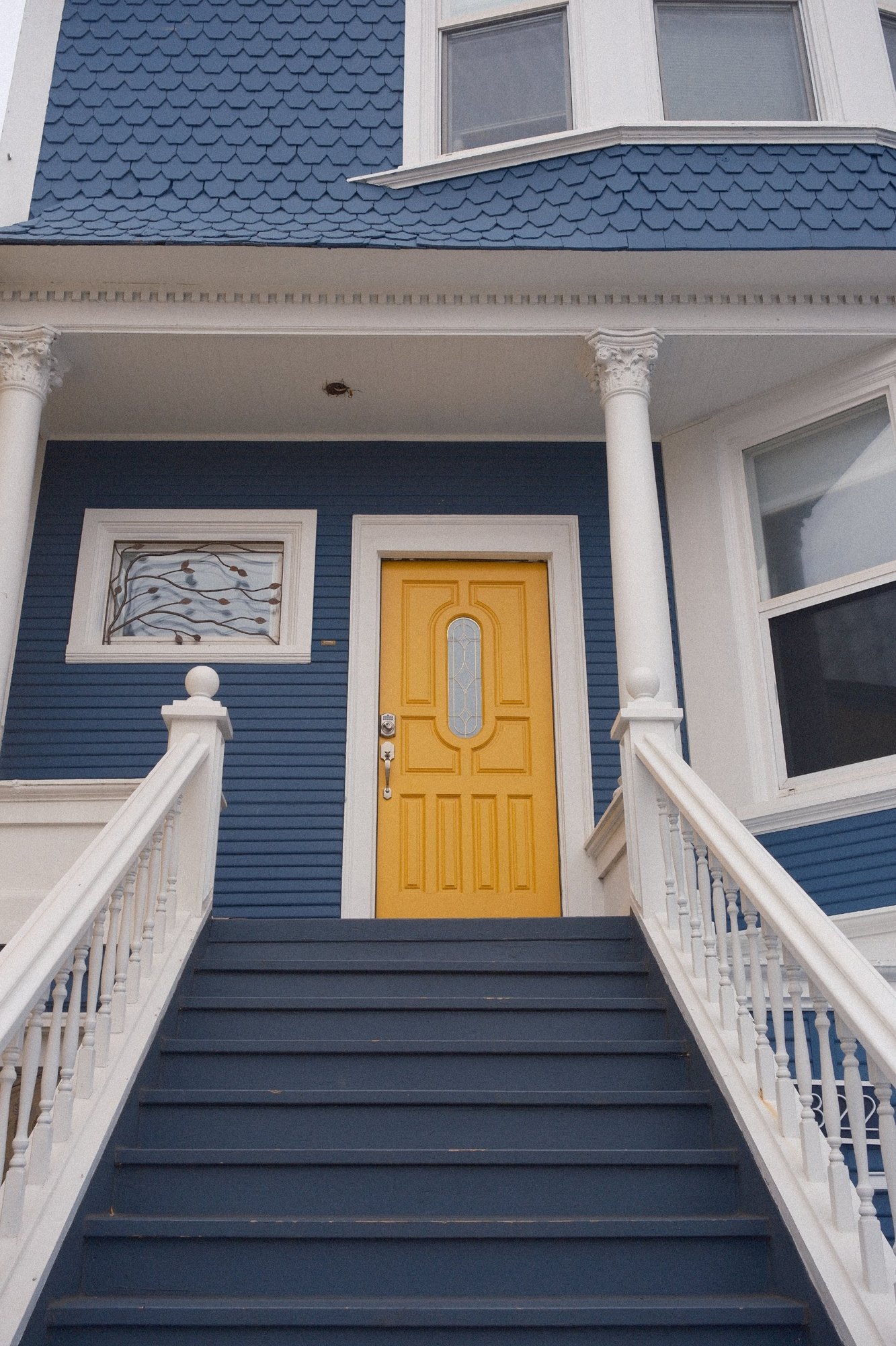 A mustard front door at the top of navy steps on a blue Victorian