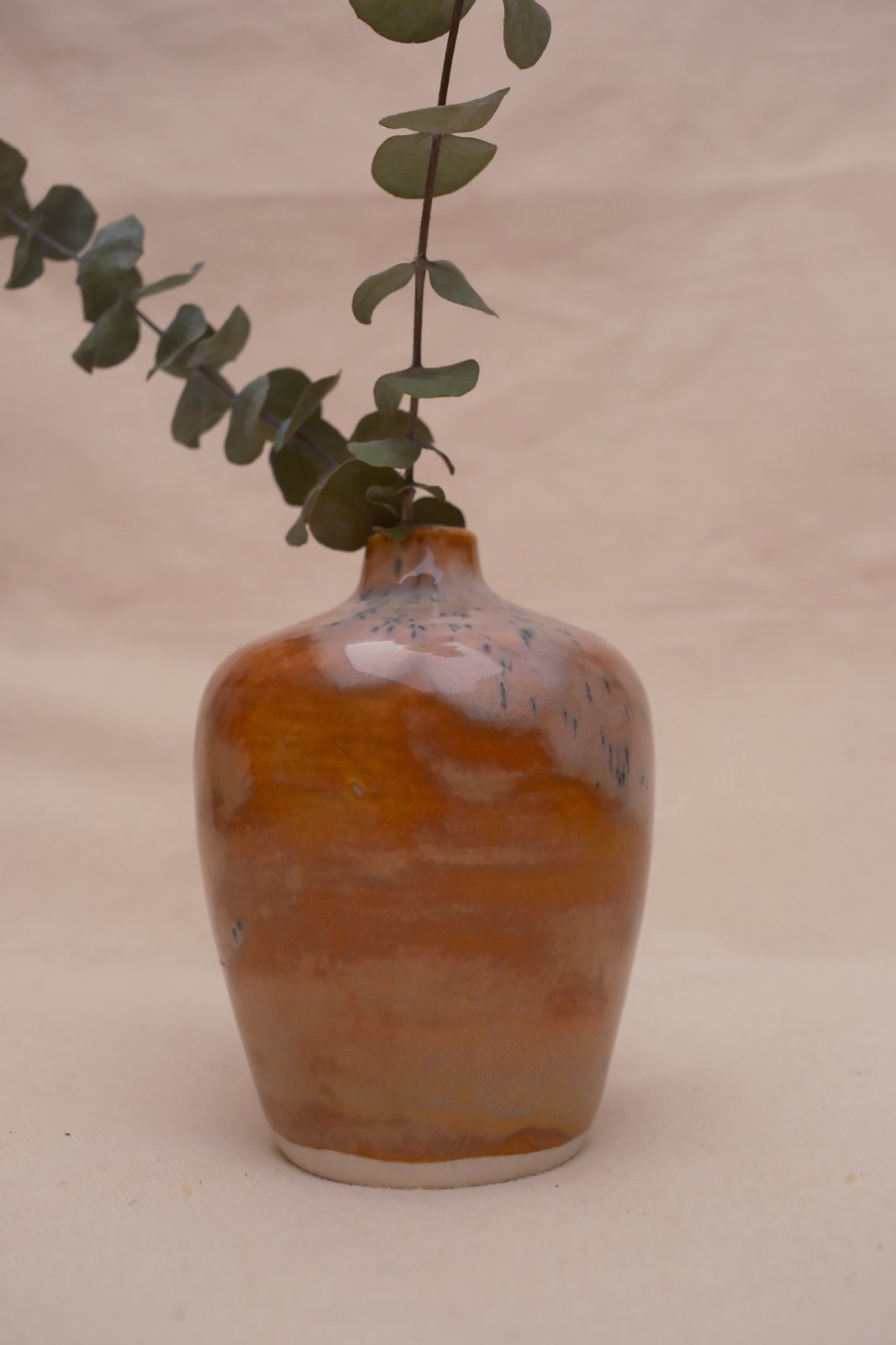 Close view of the vase with eucalyptus, orange glaze glowing under the white