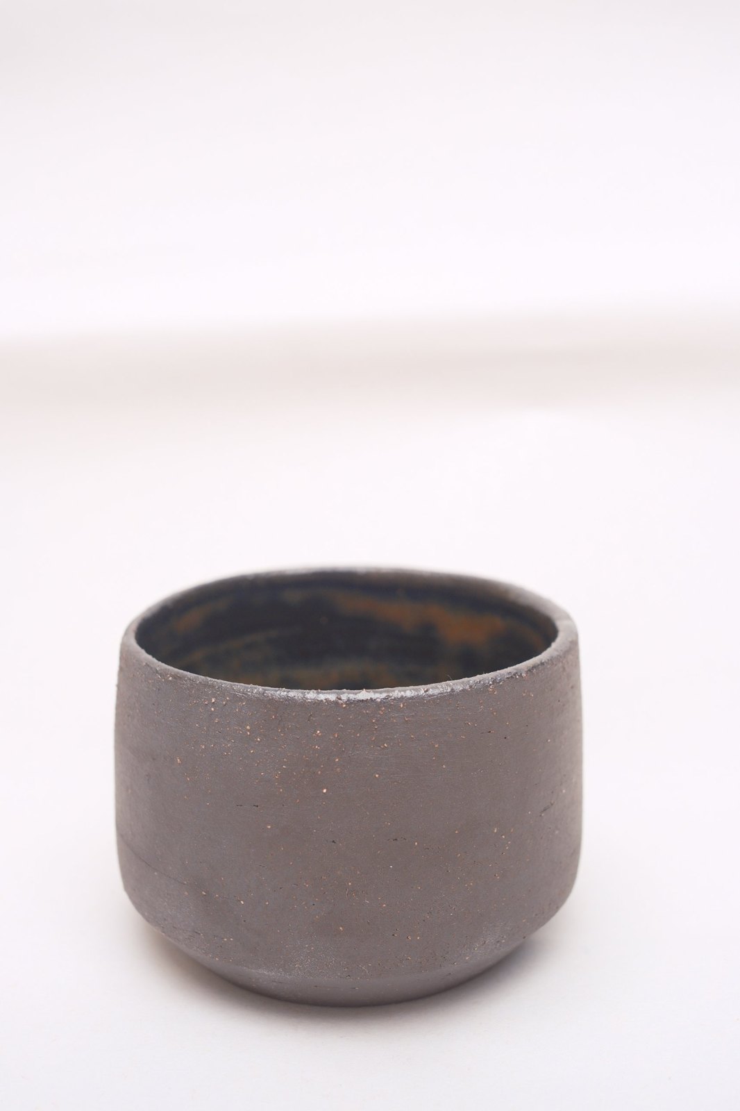 Short espresso cup in raw dark brown clay, on a pale backdrop