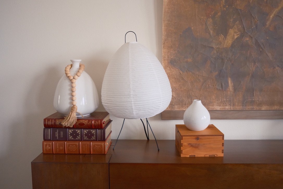 Paper lantern lamp between a white vase on leather-bound books and a small bud vase