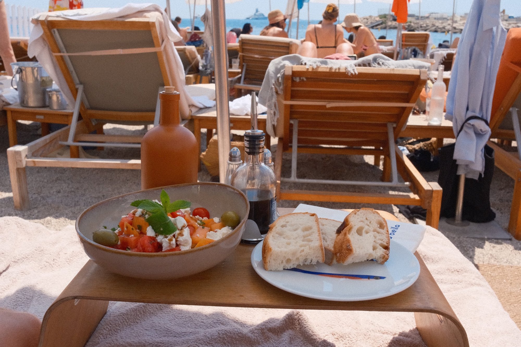 Melon and feta salad with bread on a beach-club lounger, the sea beyond