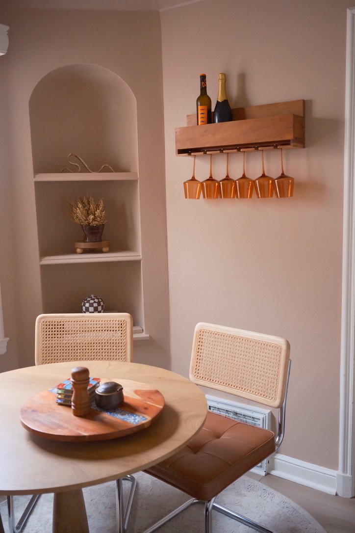 Cane chairs at a round table beside an arched niche and a wall rack of amber glasses