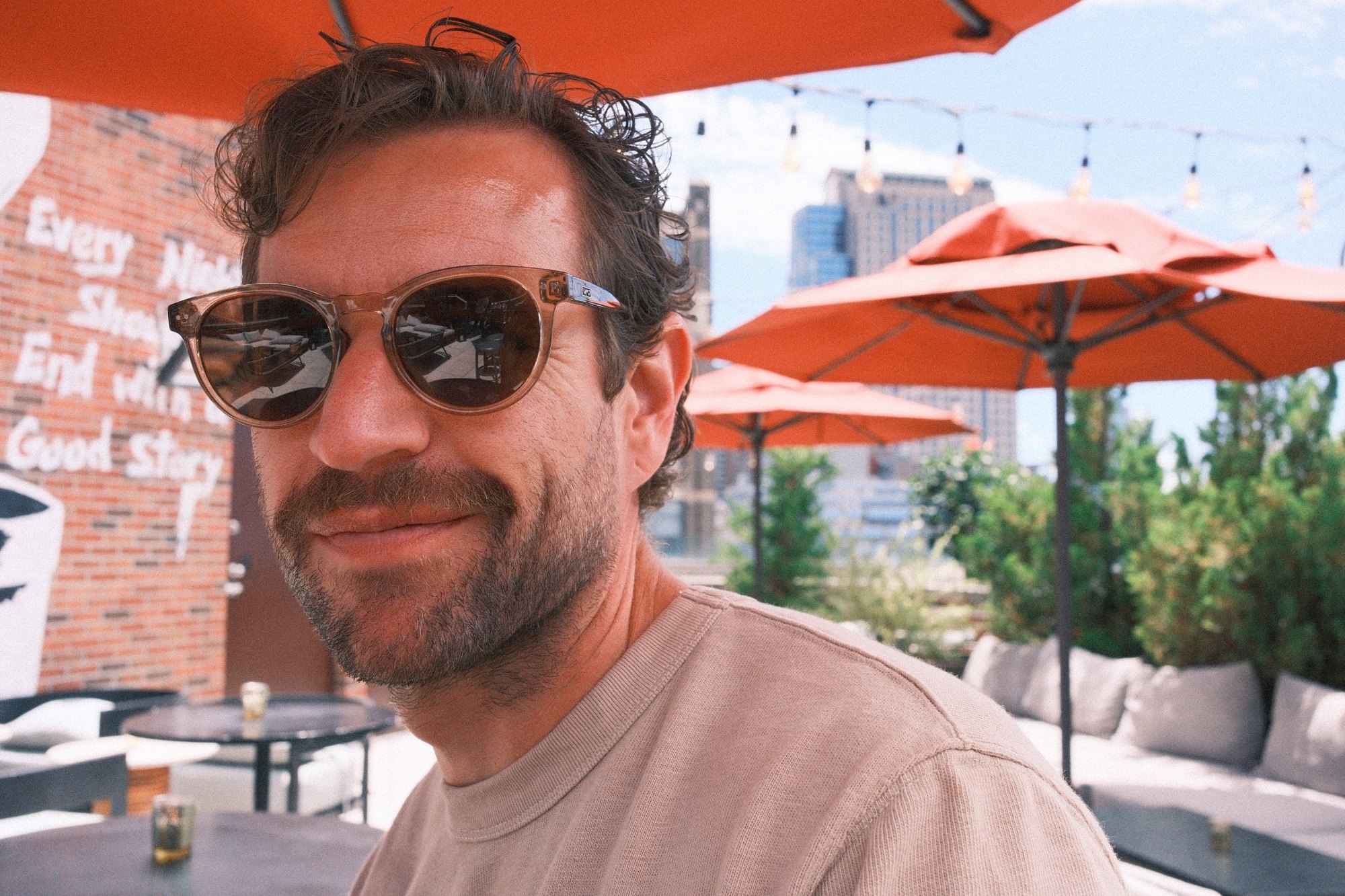Rooftop portrait in tortoiseshell sunglasses under orange umbrellas