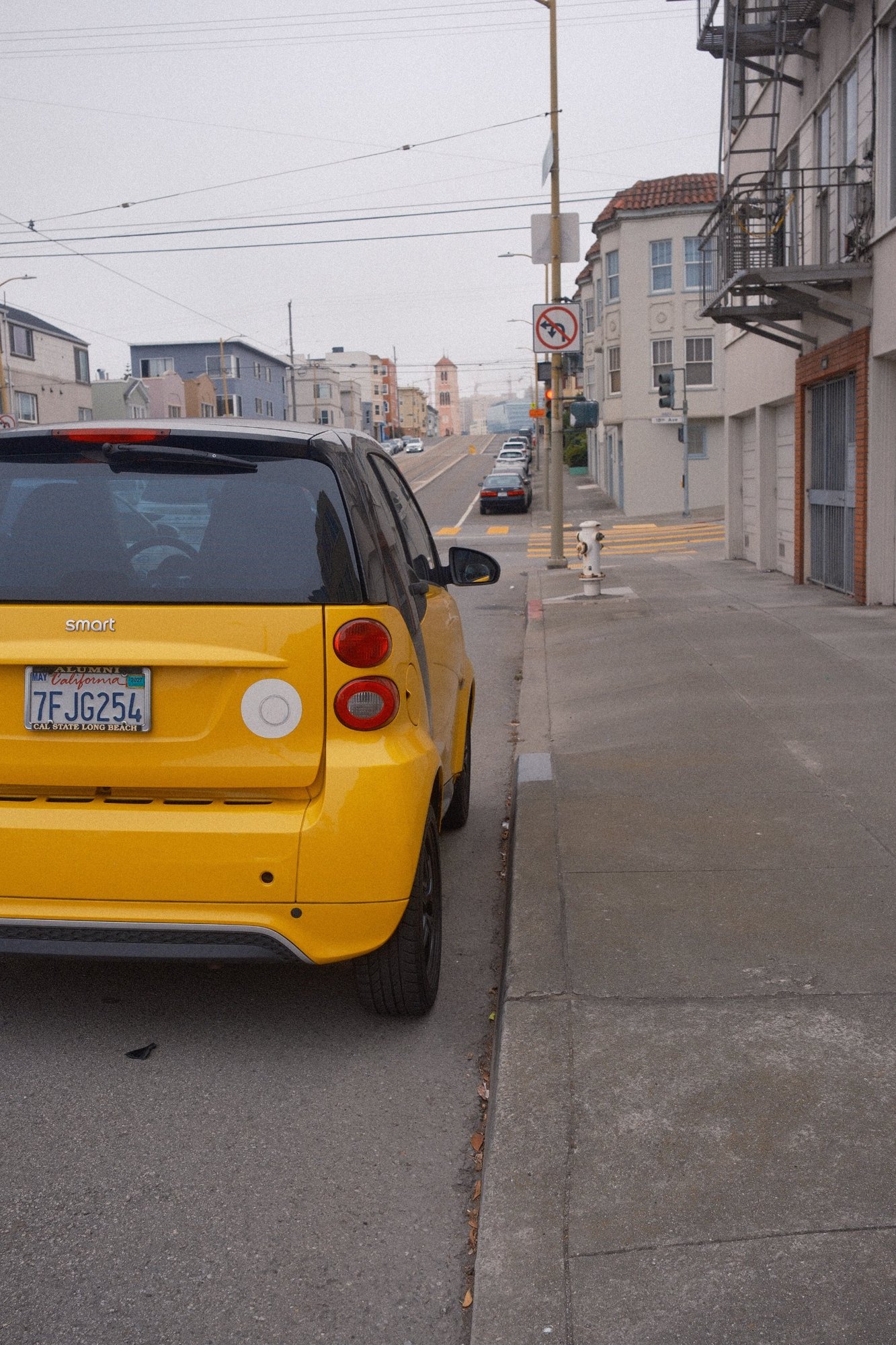 A little yellow Smart car parked on a hill of pastel houses