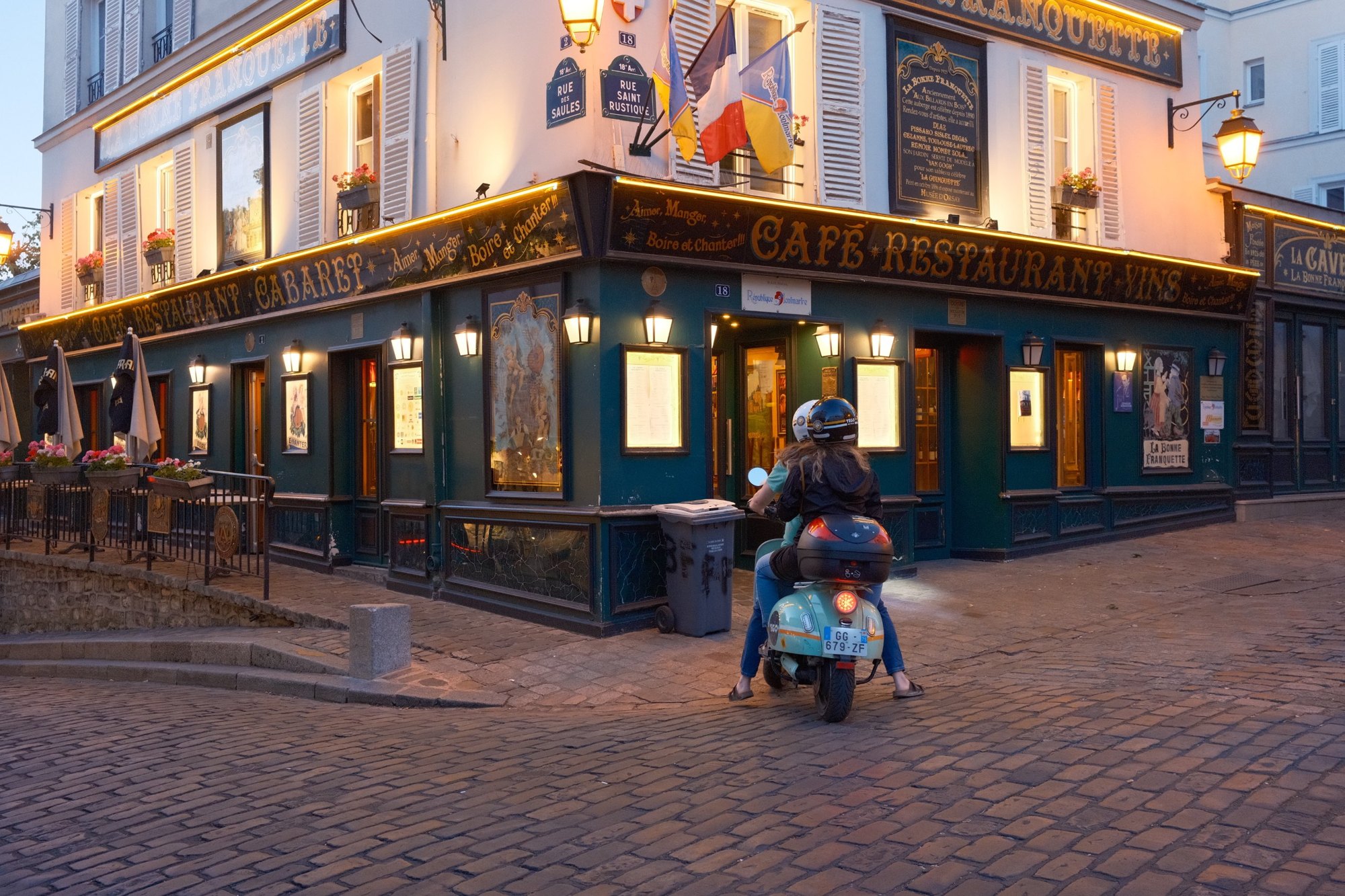 La Bonne Franquette's gilded signs lit up over cobblestones, a scooter waiting at the corner
