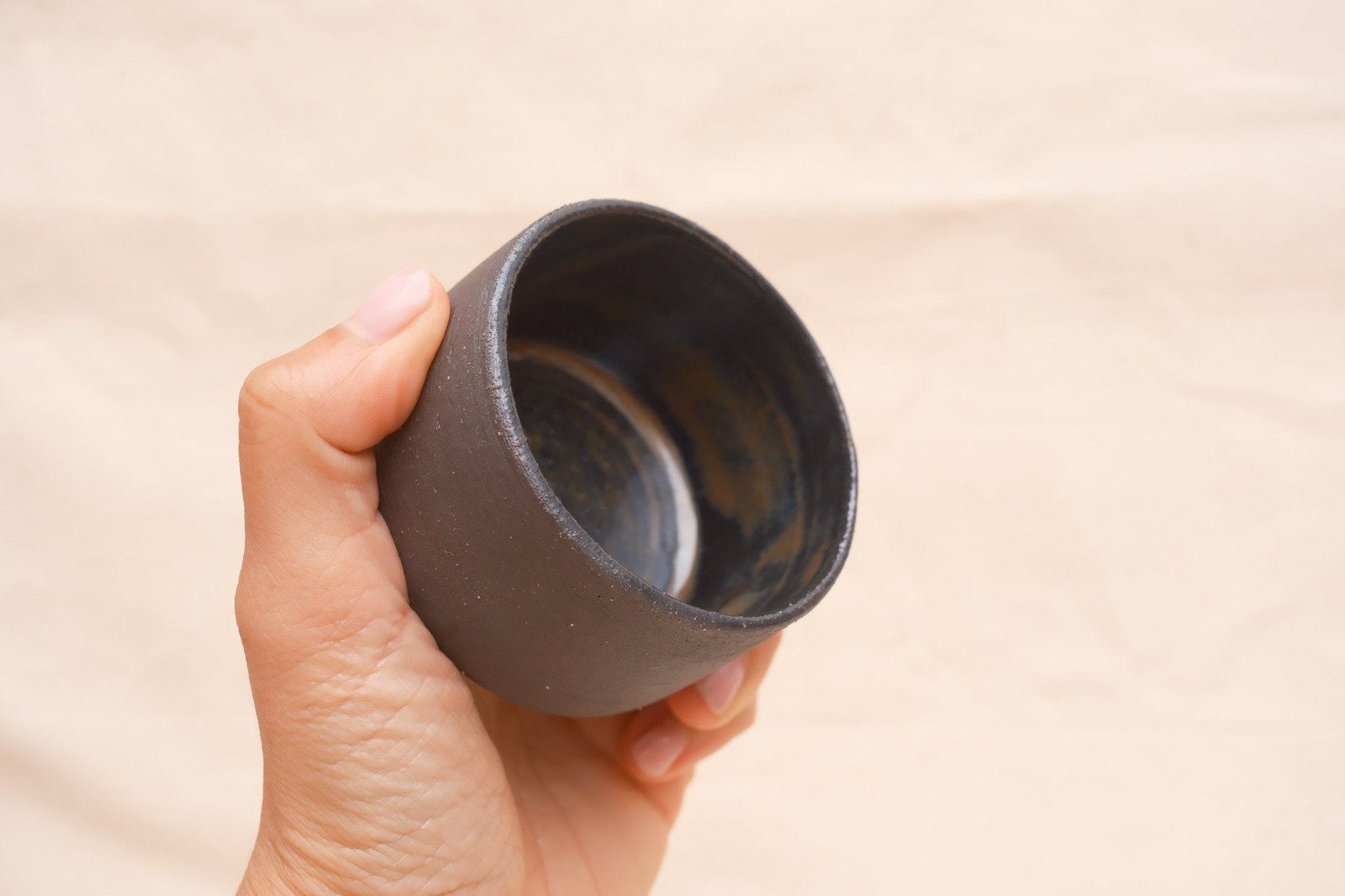 The cup cradled in a hand, rust and blue glaze inside