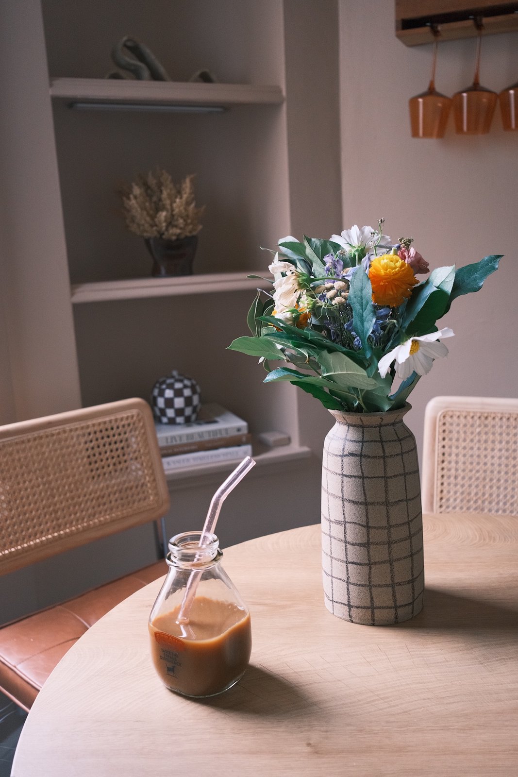 Garden flowers in a grid-painted stoneware vase on an oak table