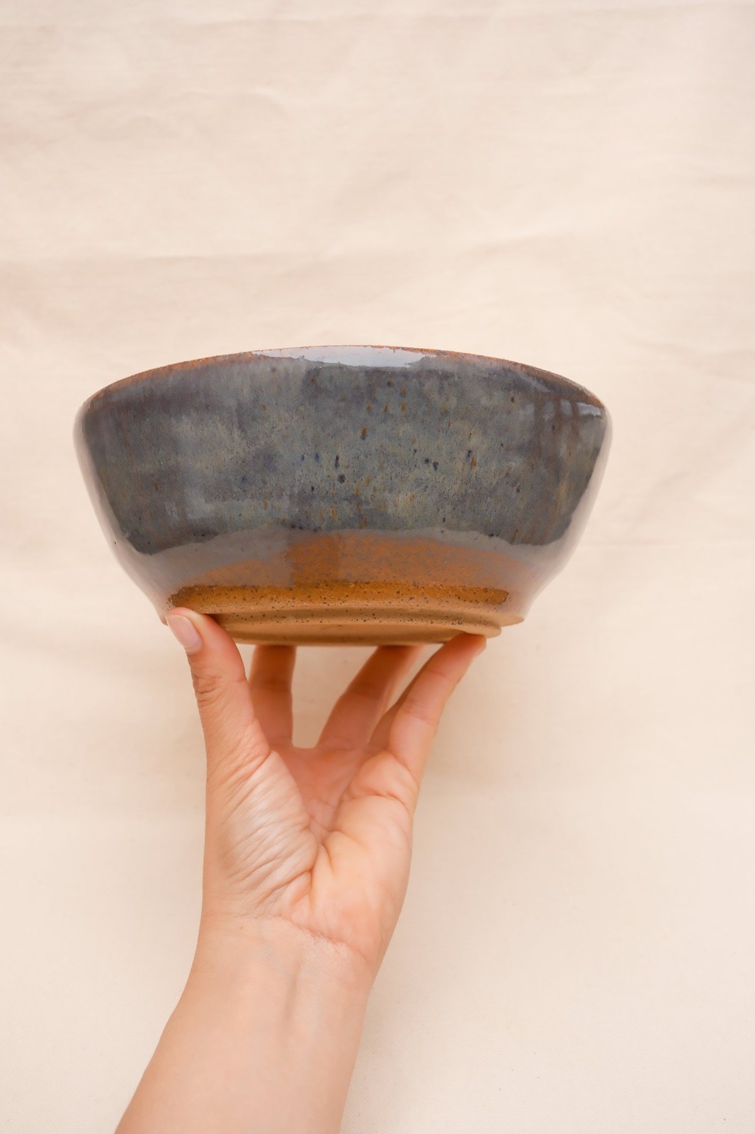 The bowl balanced on a hand, glaze breaking to rust above the foot