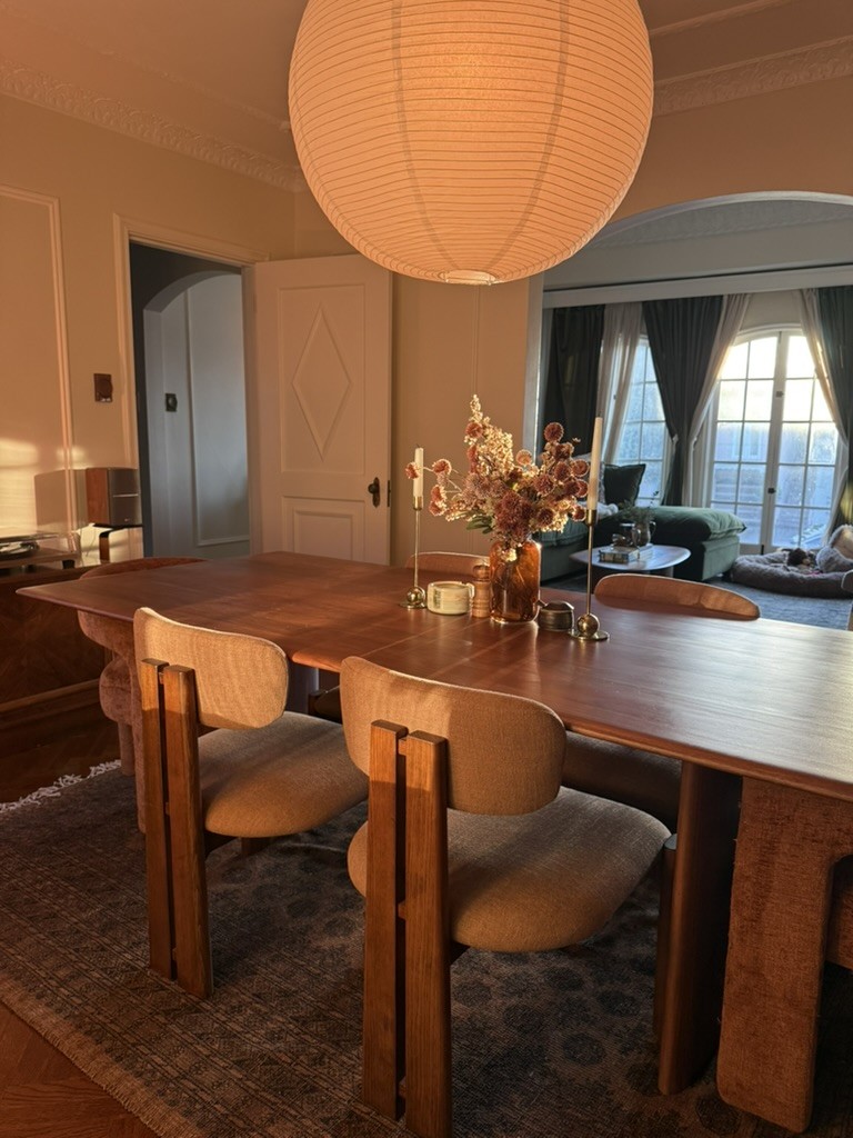 Sanoma's dining room in golden-hour light: walnut table, upholstered chairs and a paper lantern