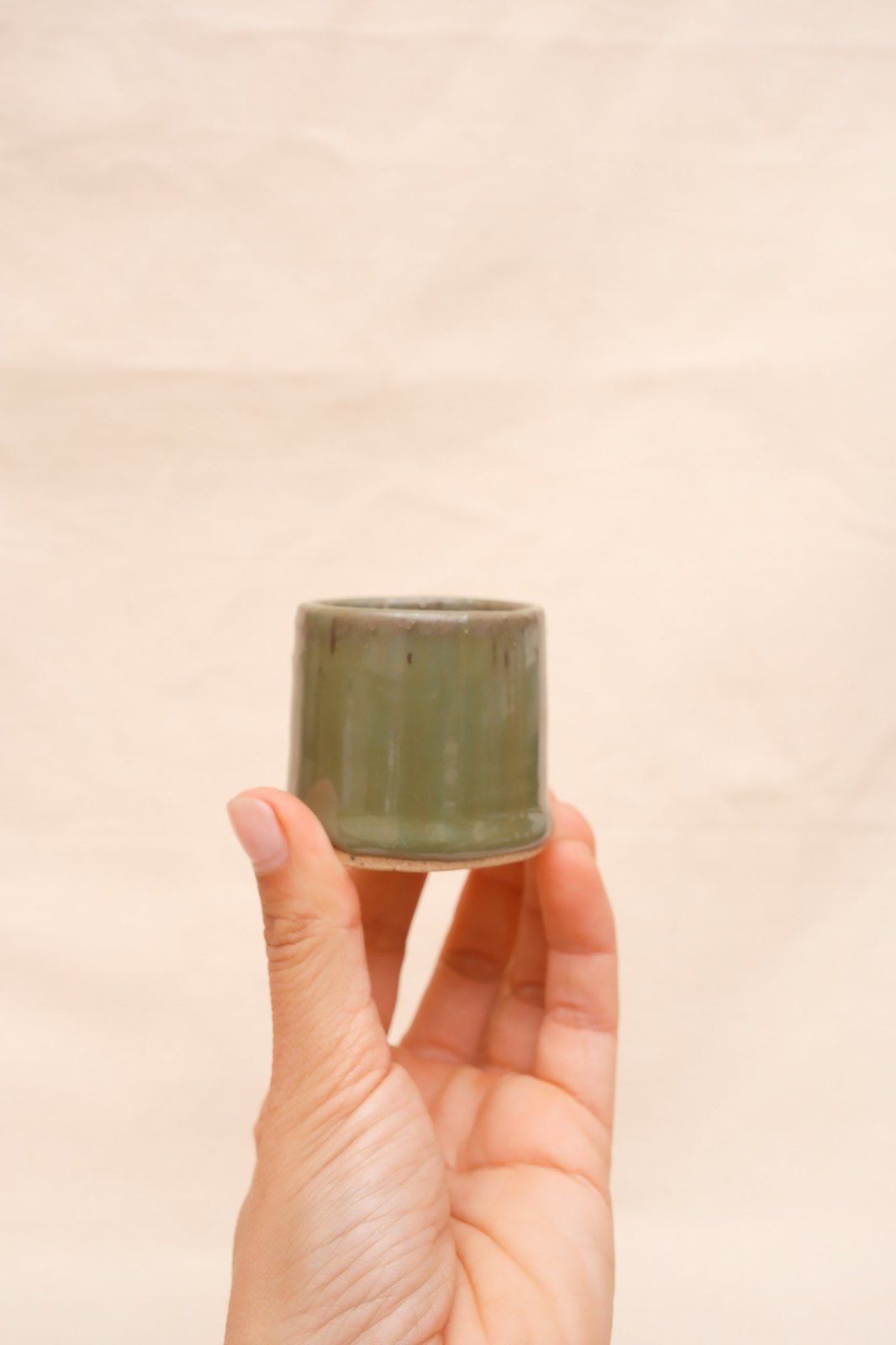 One shot glass held up between thumb and fingers, showing its size