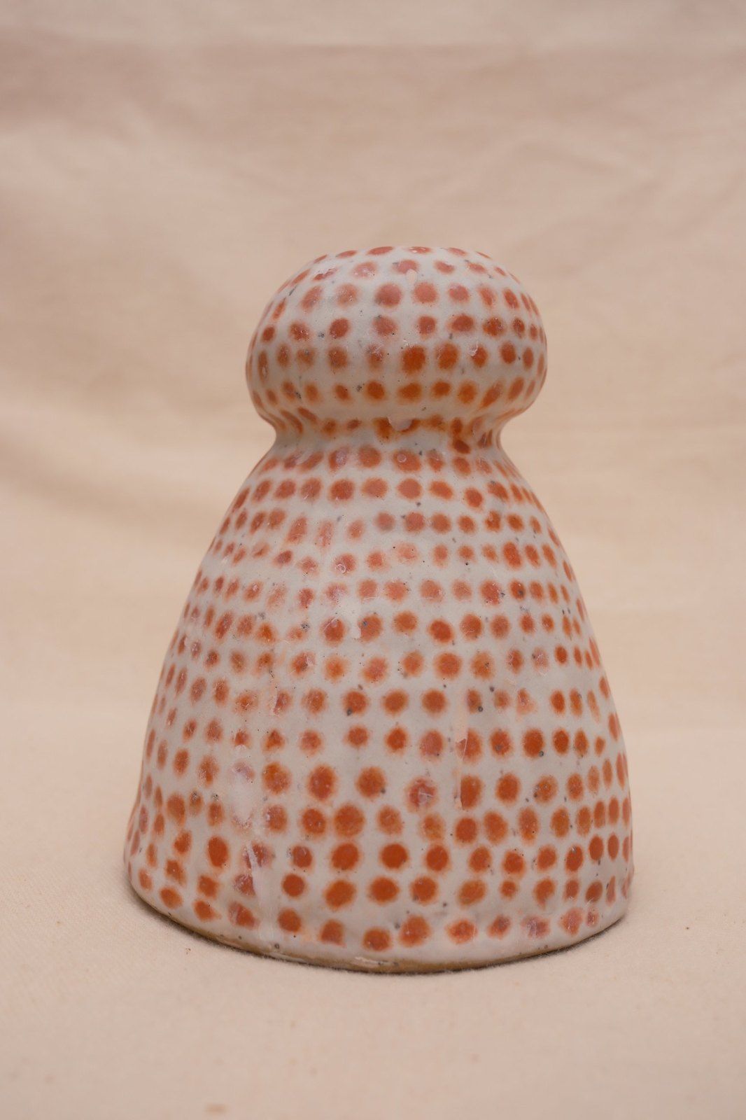 Handmade porcelain vase covered in orange dots, on linen