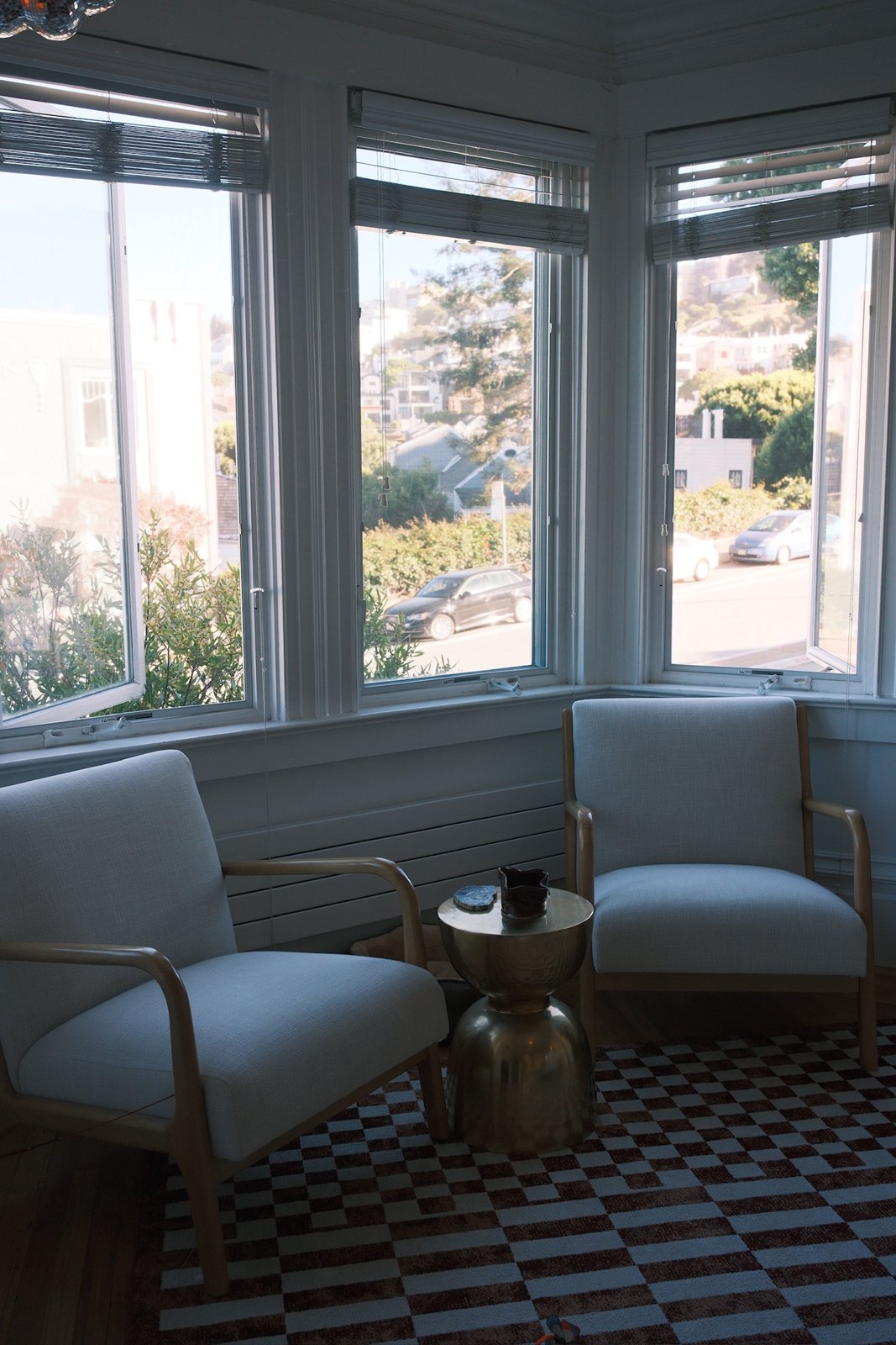 Two linen armchairs and a brass side table in a bay window