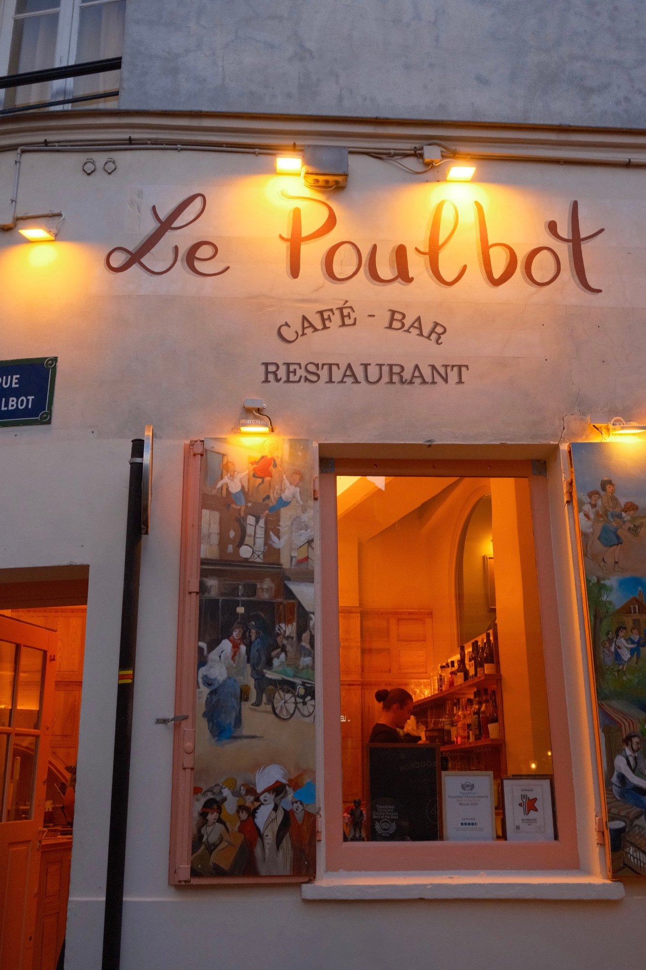 Le Poulbot's hand-lettered sign glowing above painted shutters