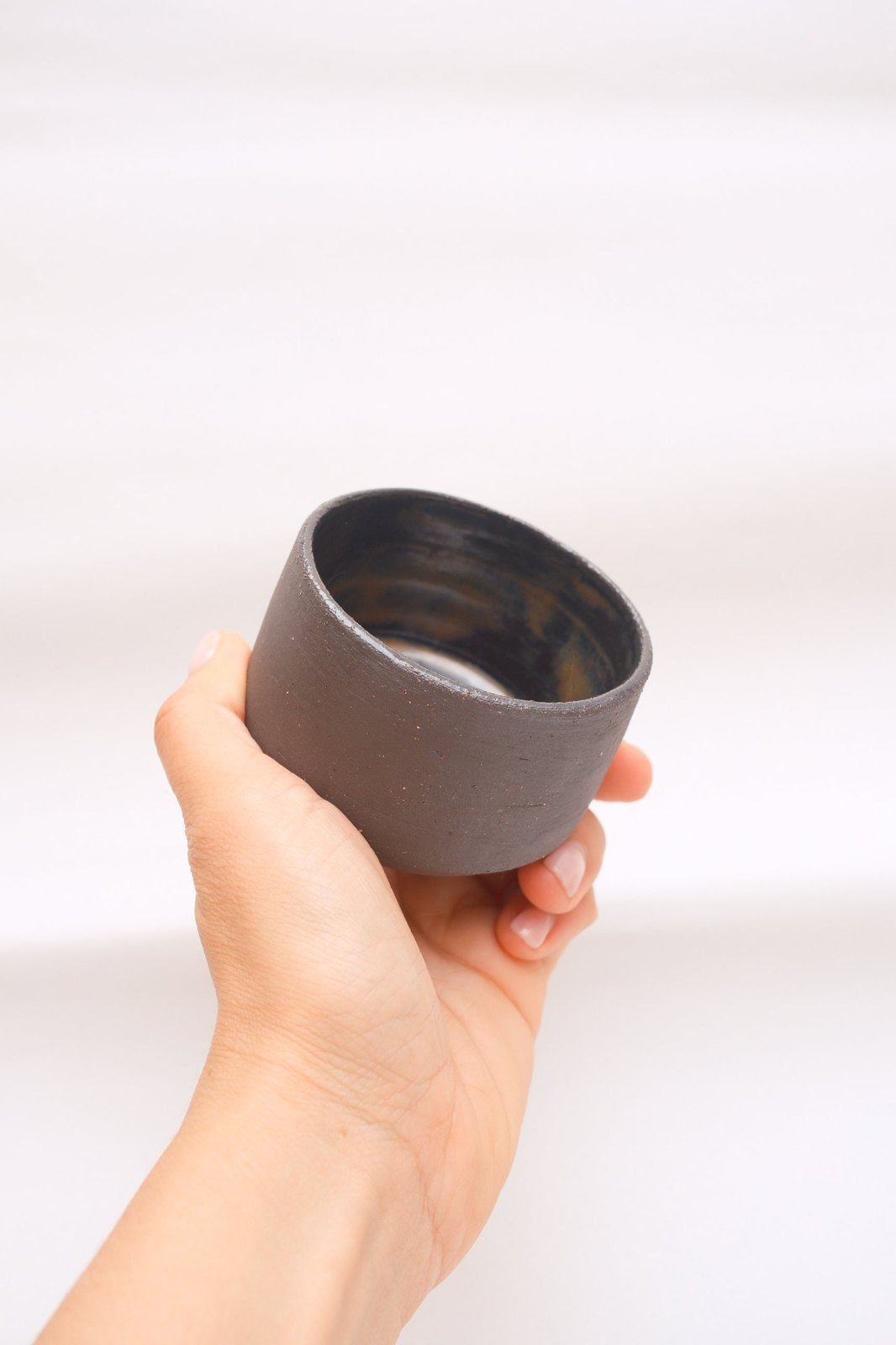 The cup held in one hand, glossy glaze swirling inside