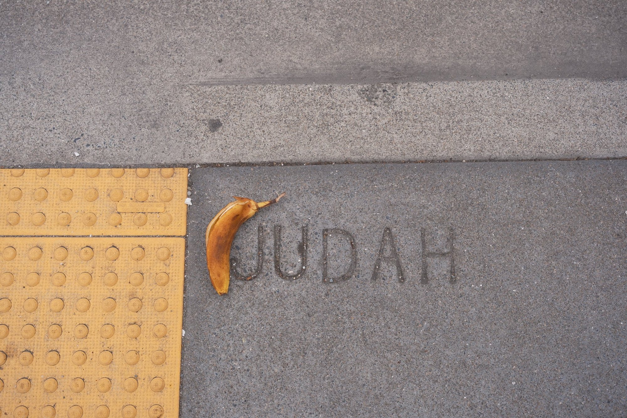 A banana peel curling into the J of JUDAH stamped in the sidewalk