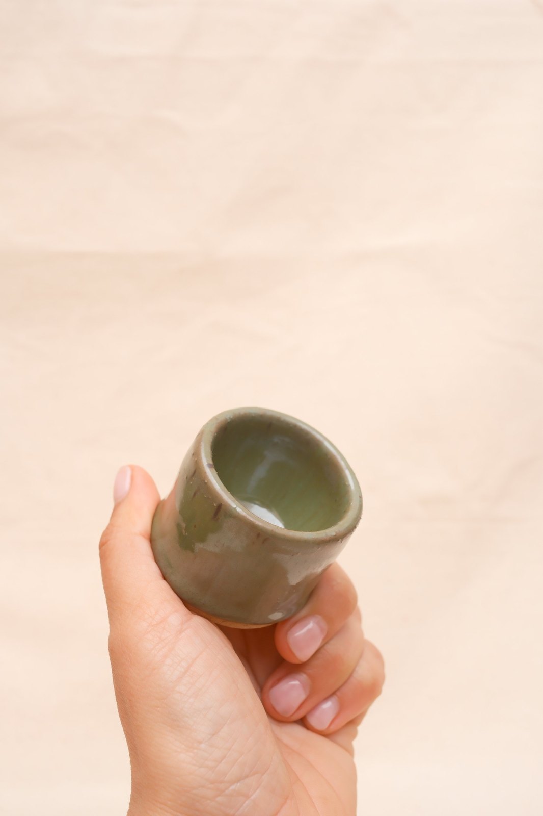 A shot glass cradled in a hand, rim speckles visible