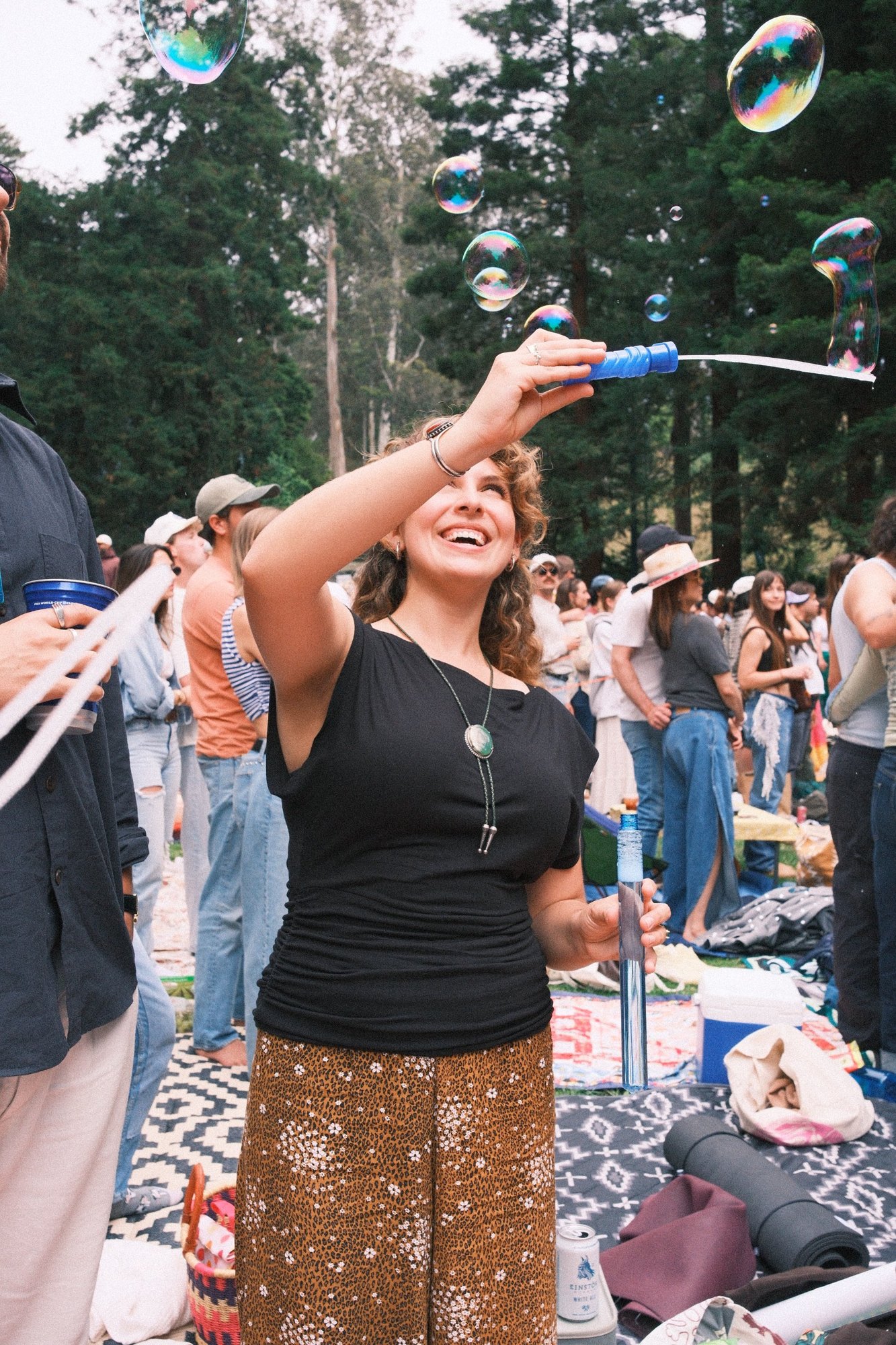 A woman laughing as she blows giant bubbles at Stern Grove, a bolo tie at her neck
