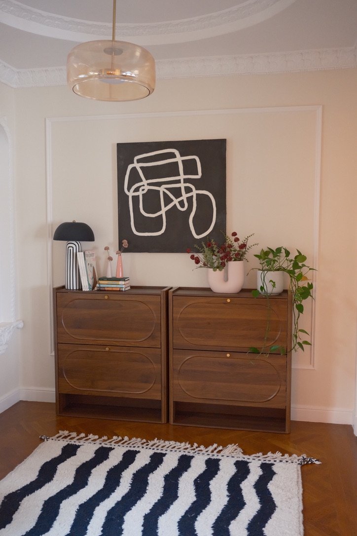 Walnut cabinets styled with a mushroom lamp, books and plants under abstract black-and-white art