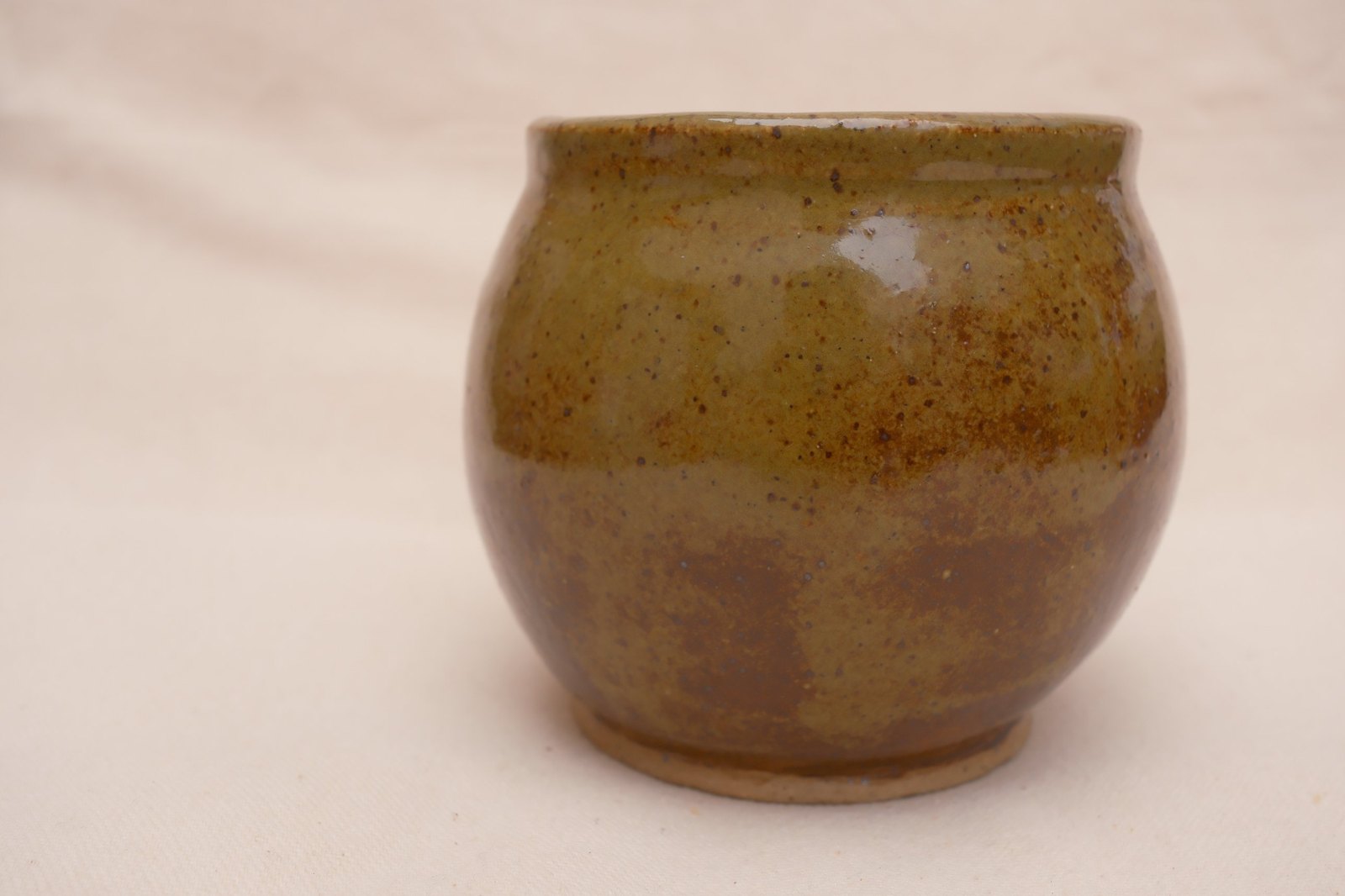 Close side view of the olive glaze fading to rust, speckles throughout