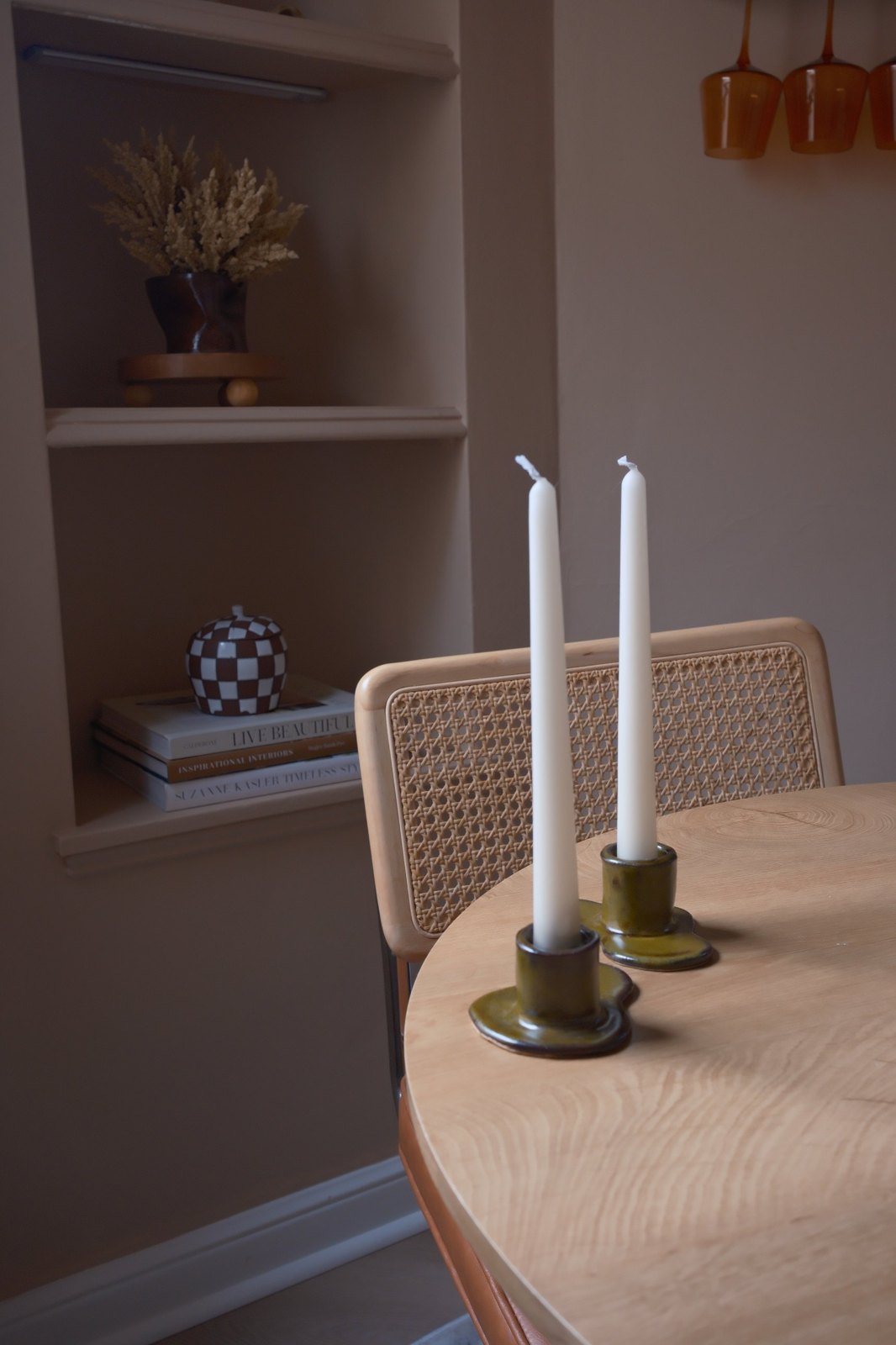 The candlestick holders styled on a light wood dining table beside a cane-back chair