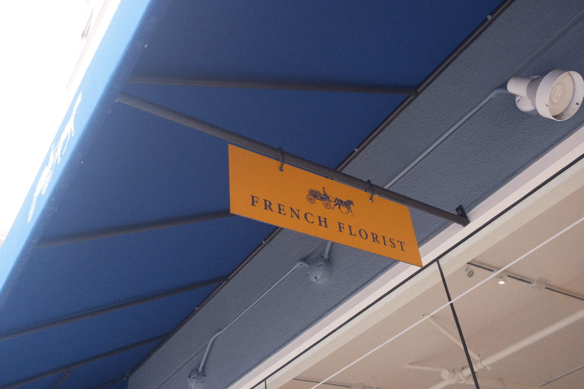 A mustard French Florist sign under a cobalt awning