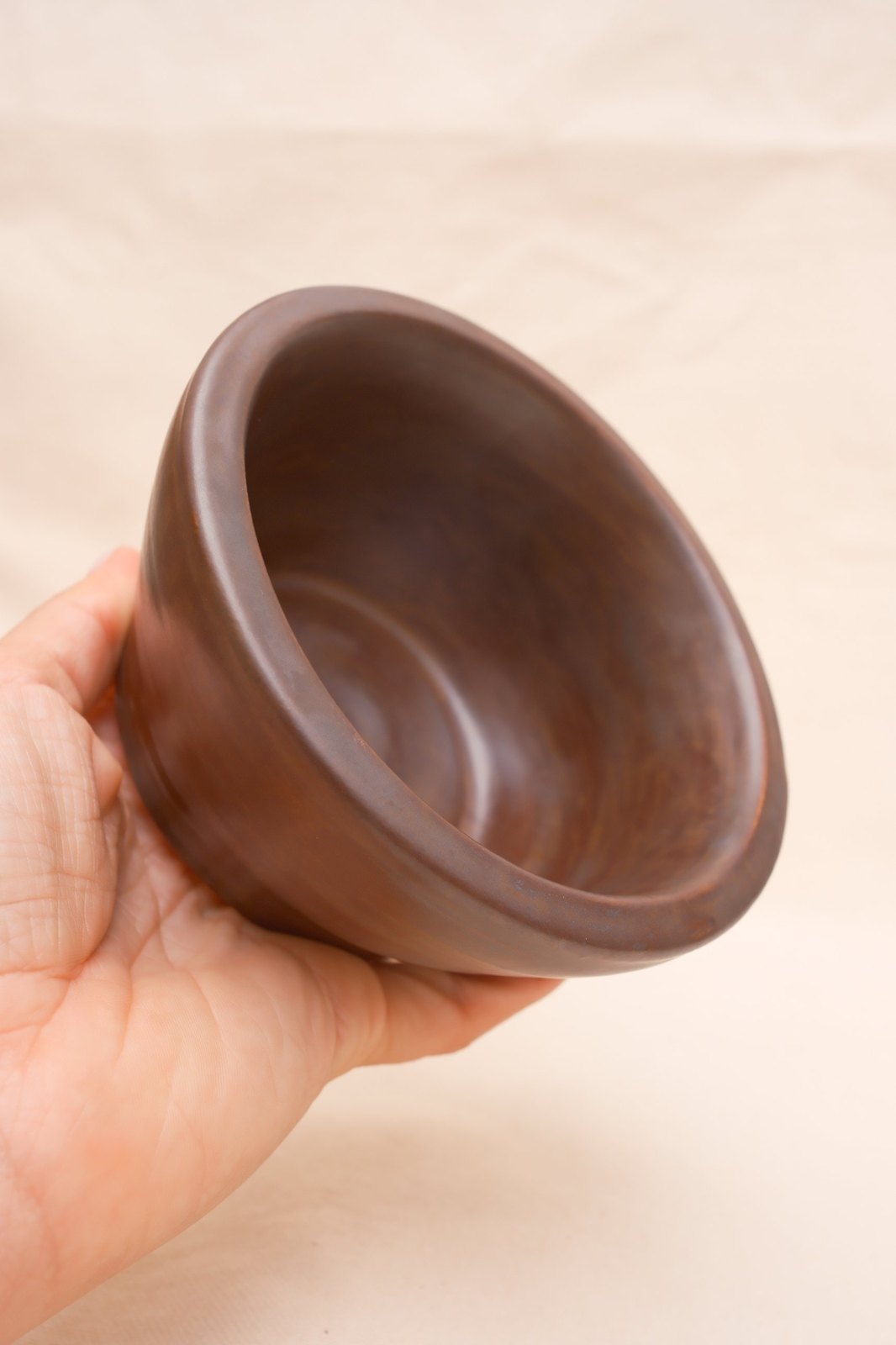 The bowl tipped in the hand, showing the thick rolled rim
