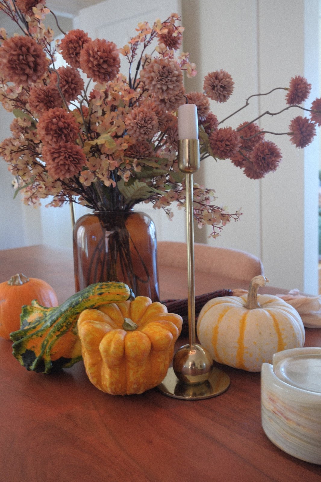 Closer view of the fall table: gourds, a white pumpkin and a slim brass candlestick