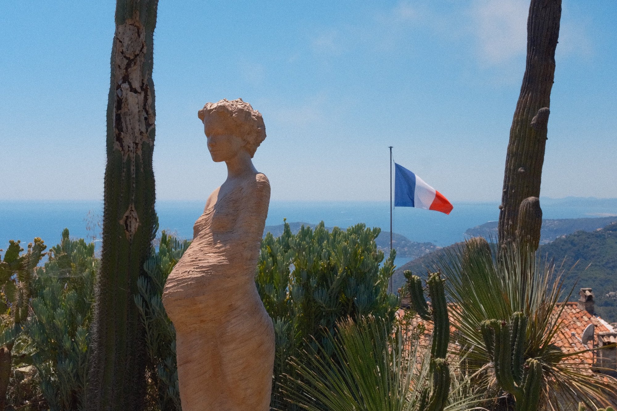 A terracotta statue among cacti, the tricolore and the coast behind
