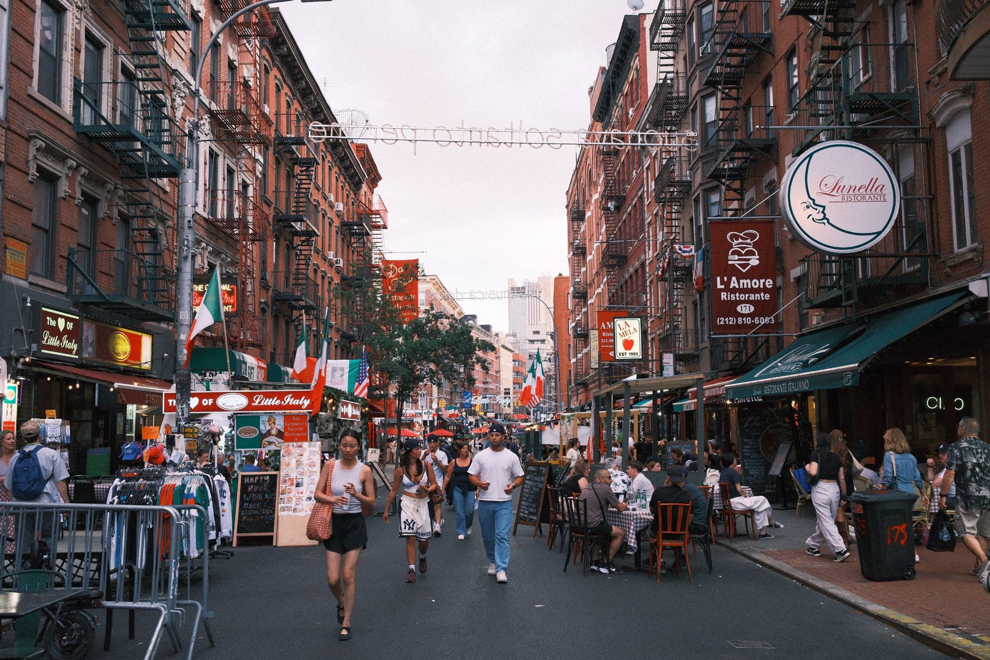 Mulberry Street closed to cars: diners, flags and fire escapes under a string-light sign