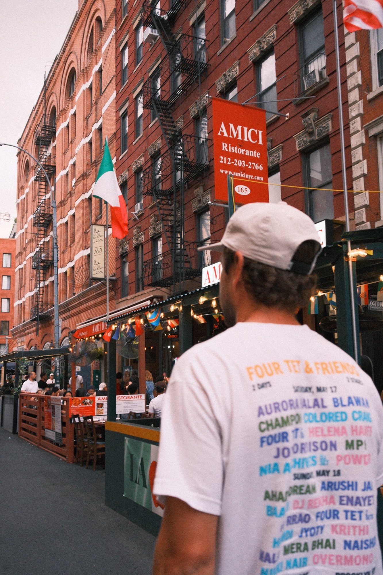 A festival T-shirt from behind, looking up at the red Amici Ristorante banner
