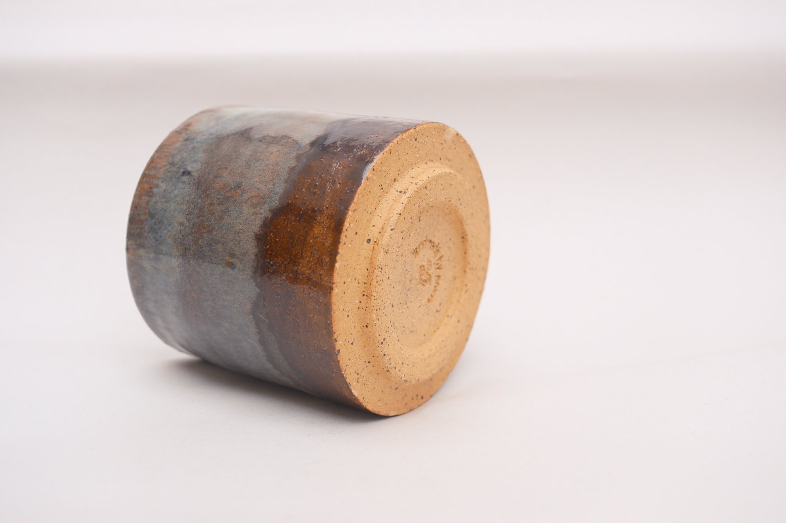 Underside of a cup: bare speckled clay foot with a maker's stamp